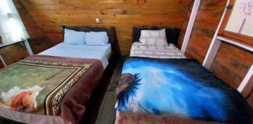 Interior con dos camas matrimoniales en cabaña pequeña.