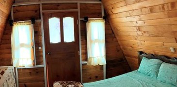 Interior de madera con cama, puerta y ventanas.